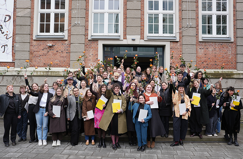 70 Personen posieren auf einer Treppe für ein Gruppenbild und halten Rosen in den Händen