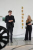 Vor Malereien stehen zwei Personen in einem Ausstellungsraum