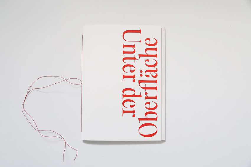 Das Bild zeit ein weißes Buch mit roter Schrift: "Unter der Oberfläche" steht auf dem Buchcover